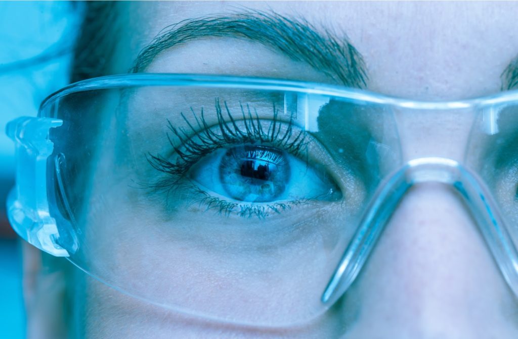 A woman wearing safety glasses showing primarily  the lens of the eyewear