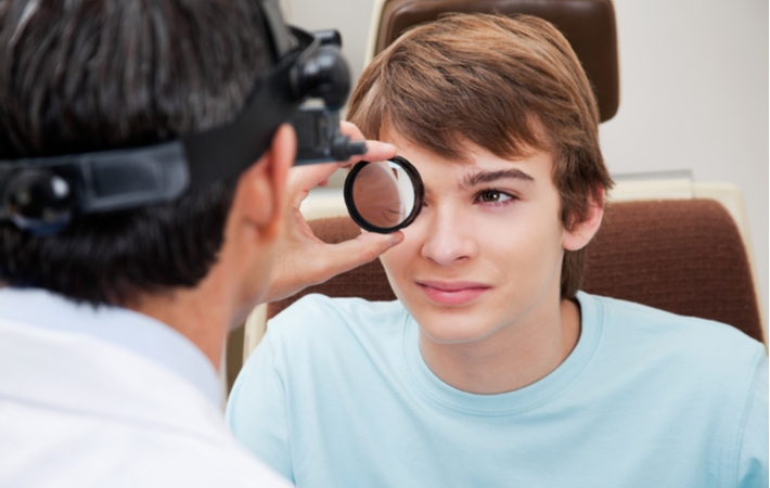 An optometrist magnifying a teenage boys eye to take a closer look during a dilated eye exam