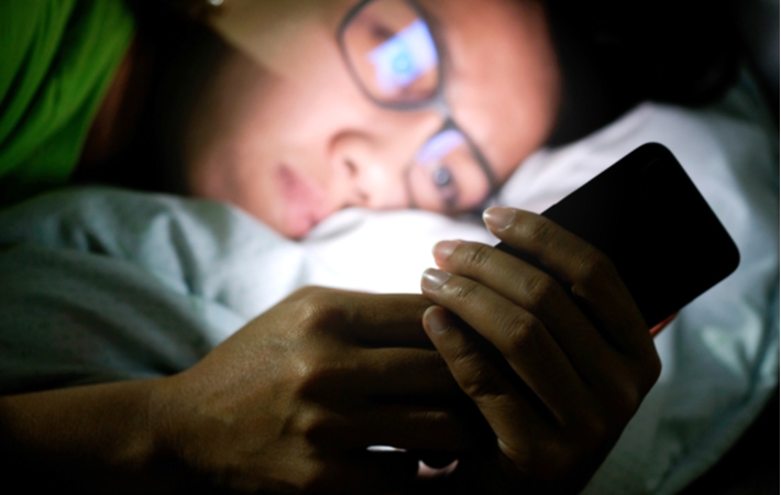 A person laying down in their bed at night, looking at their phone in the darkness