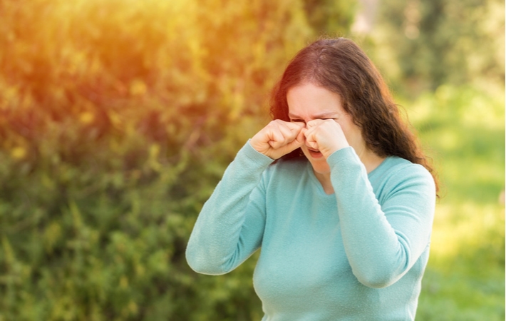 A woman standing outside rubbing her eyes in pain due to prolonged sun exposure on her eyes