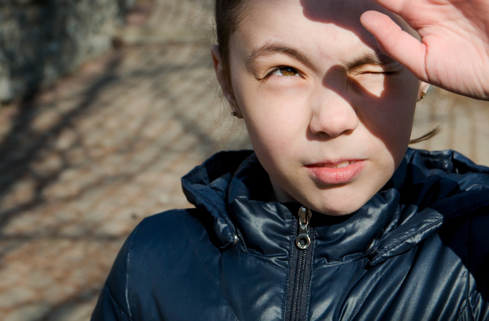 A young girl using her hand to shield her eyes from the sun outside