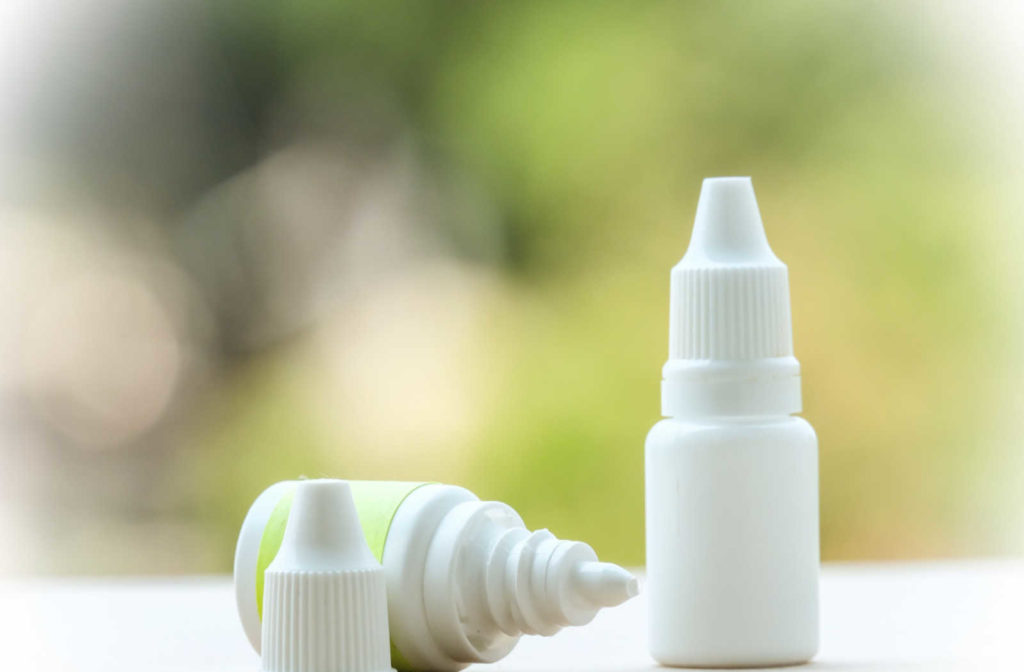 Two bottles of eyes drops on a counter, one is laying down with the lid off and the other is placed upright.