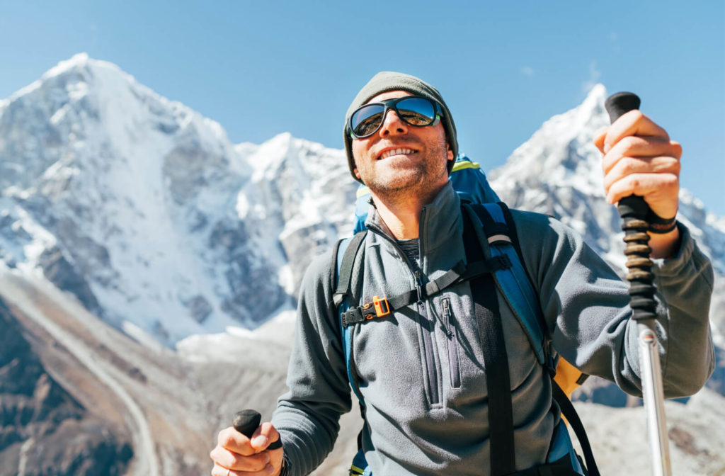 A man outside hiking a mountain while wearing UV protection sunglasses to protect his eyes